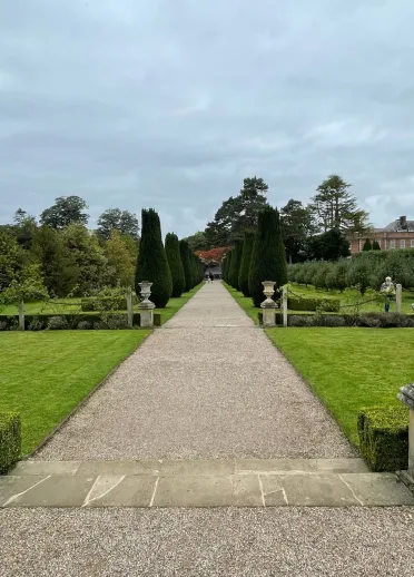 A pathway in a garden leading to a grand, historic house.
