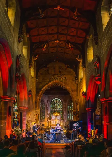 Inside of a church lit up whilst a band is playing, with an audience watching on.