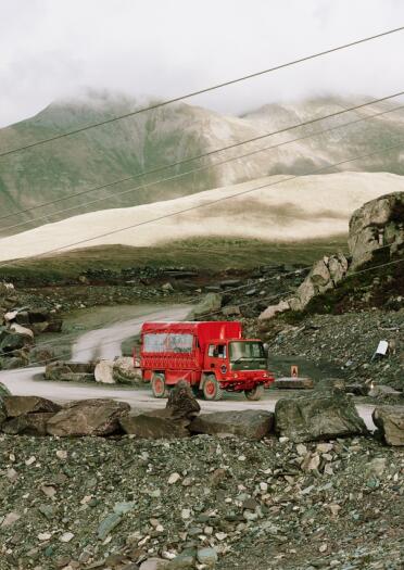 A red touring truck driving through a quarry.
