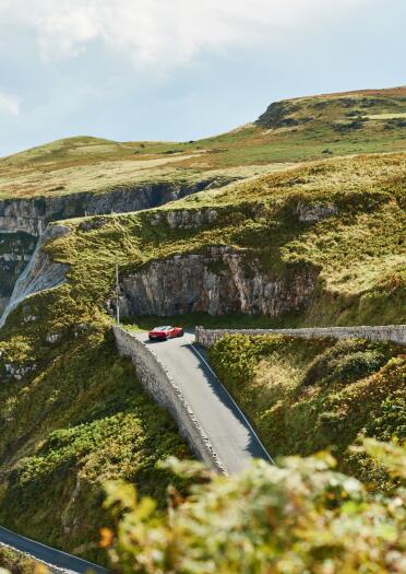 A car driving around a zig zag road on a cliff.