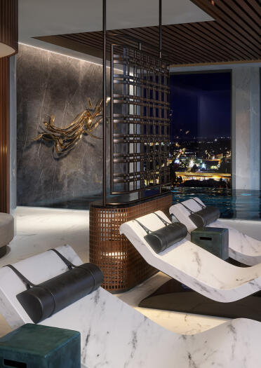Spa beds and loungers by a pool with views of the city beyond.