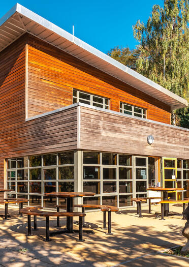 A wood panelled visitor centre surrounded by tables and seats amongst forestry.