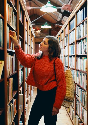 A young lady selecting a book surronded by bookshelves in Hay on Wye
