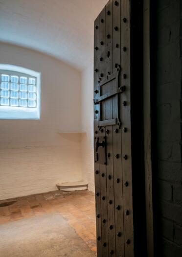 An open black prison door leading into a cell.