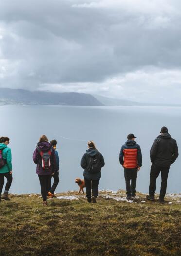 A group of people on a headland overlooking views of mountains toward the sea.