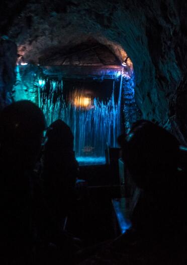 People underground on a boat approaching a lit up waterfall.
