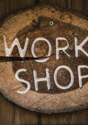 The word Workshop carved into a wooden sign on a piece of tree trunk.