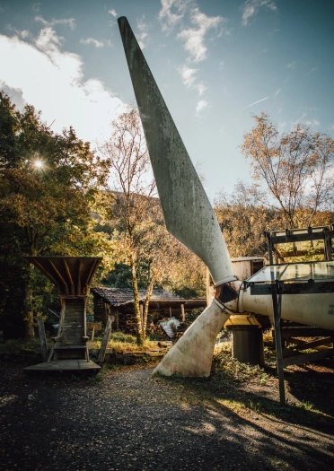 An old wind turbine on its side with a propeller buried in the ground.