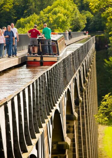 A canal boat travelling along the Pontcysyllte Aqueduct with people walking along the footpath.