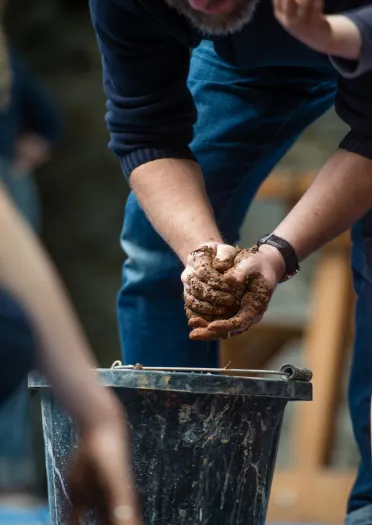 A pair of hands moulding clay from a bucket at Centre for Alternative Technology.