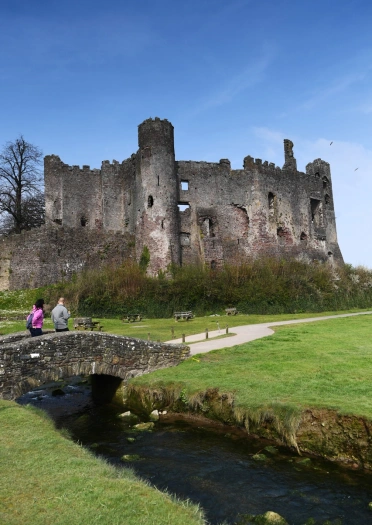 People walking on a footbridge over a steam towards a castle.