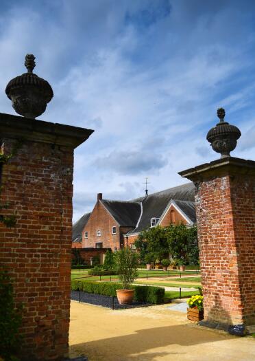 A stately home and gardens through seen through two brick gate posts.