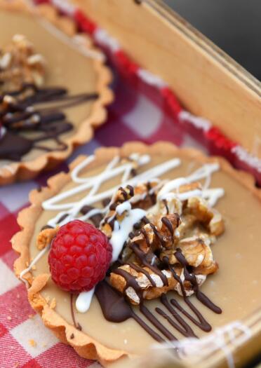 Two pastry tarts decorated with walnuts, a raspberry and icing in a wooden tray on a gingham cloth.