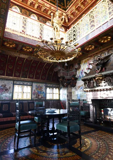 An ornate grand room with a chandelier hanging above a dining table next to a fireplace.