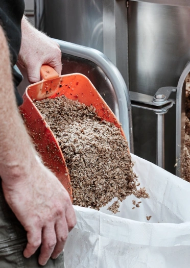 A man scooping grain from a sack into a kiln.