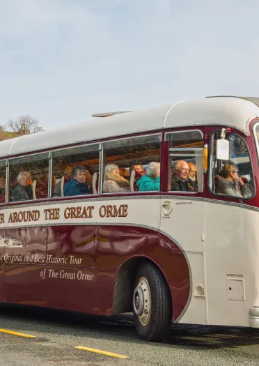 A vintage coach filled with people on a coastal road.