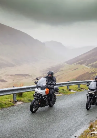 Two motorcyclists driving on a road amongst mountains.