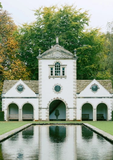 Pavilion reflected in the large pond in garden, with trees in the background.