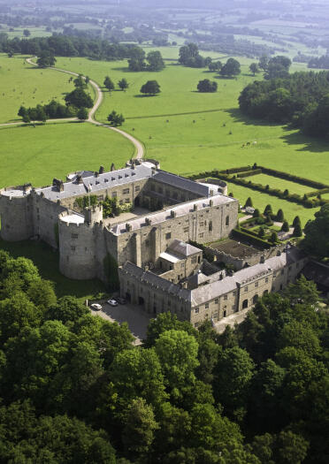 Aerial shot of Chirk Castle nestled in trees, with the valley beyond.
