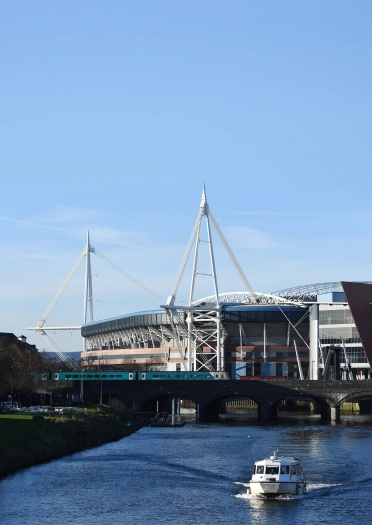 A river with a boat and a large sports stadium behind.
