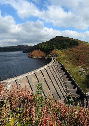 An eye level view of a dam holding back the reservoirsurrounded by a green landscape.