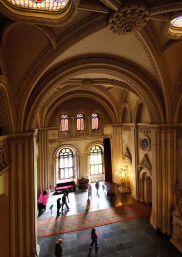 Shot from above of the interior structure and visitors at Penrhyn Castle with sunlight coming through the window.