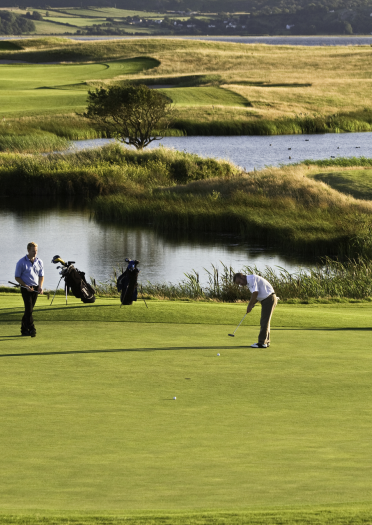 Golfers on the green with lakes in the background at Machynys Peninsula Golf and Country Club.
