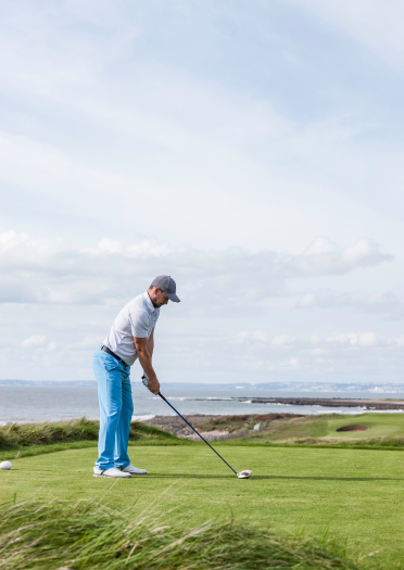 Golfer about to tee off with Porthcawl coastline in the foreground.