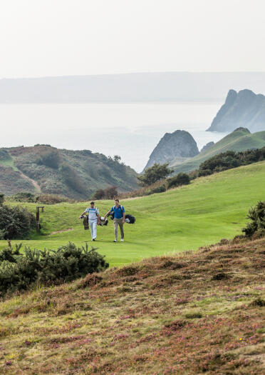 Golfers walking to their next hole at Pennard Golf Club with coastal views in the background.