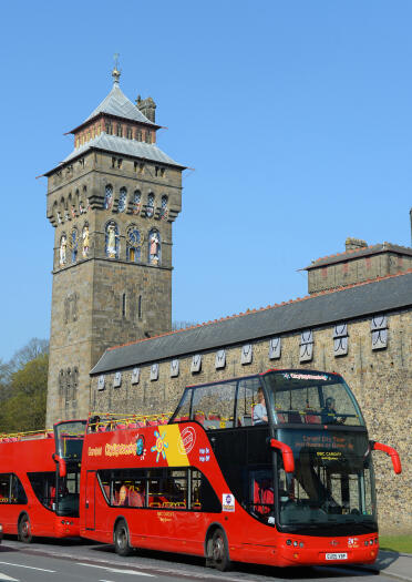 Open top sightseeing bus outside Cardiff castle with clock tower.