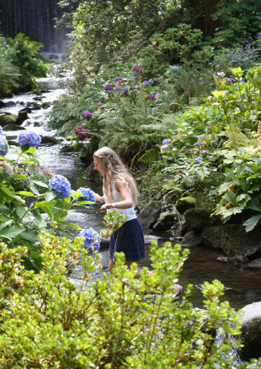 Two people crossing a stream on stepping stones in ornamental gardens.