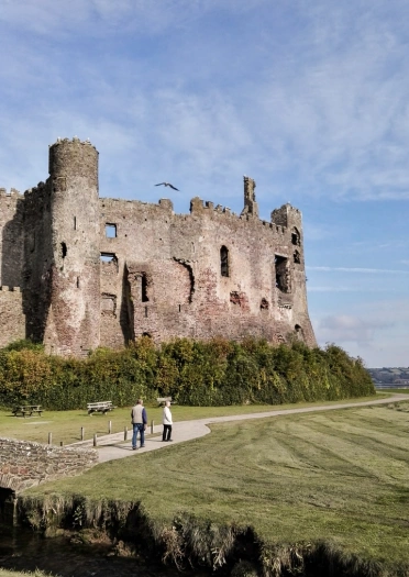 Two people walking on a path that runs past Castle ruins