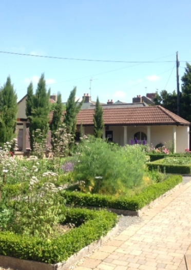 A garden with square hedge-lined beds filled with plants and wide stone paths.