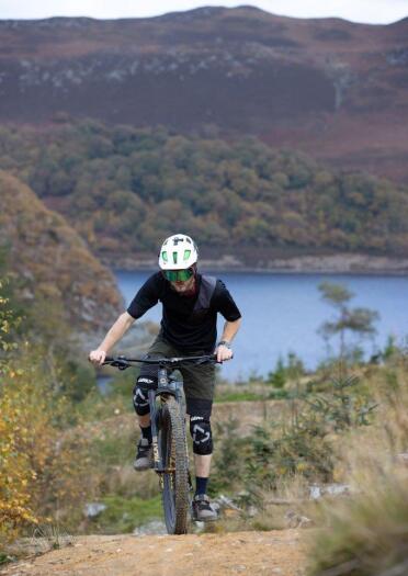 A mountain biker cycling uphill on a dirt track with mountains beyond.