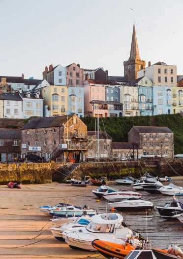 Boats moored in a harbour on a sandy beach with a path leading up to colourful houses.