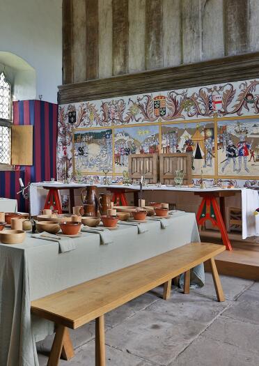 A medieval dining tables in a hall with a decorative mural.