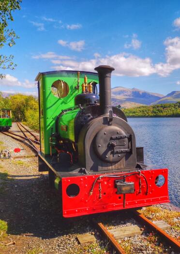 A steam train travelling past a lake and mountains.