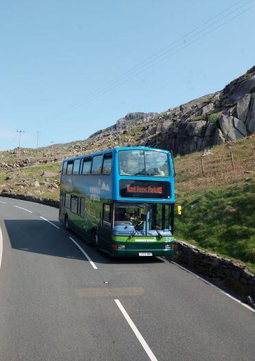 A double decker public service bus driving along mountainous scenery.
