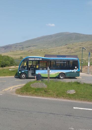 A bus waiting at a bus stop surrounded by dramatic mountains and lake.