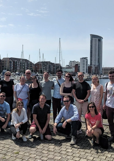 A group of people smiling at the camera by a marina.