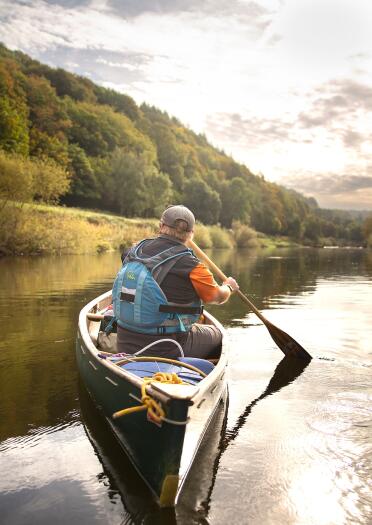A canoeist on a river surrounded by beautiful countryside.
