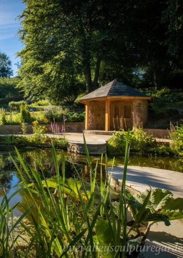 A summerhouse next to a pond surrounded by foliage.