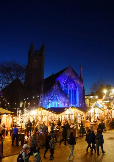 People walking around a Christmas market lit up at night with a church in the background.