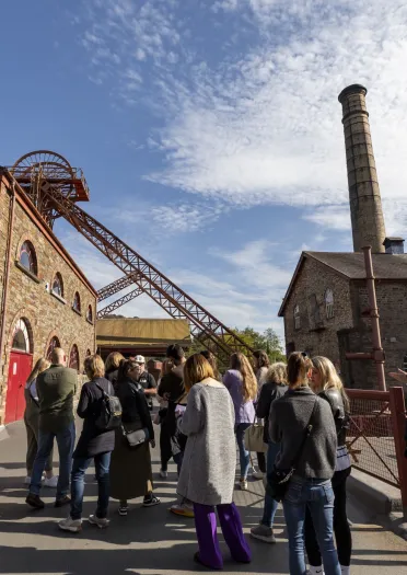 Group looking at a chimney and winding wheel at coal mining experience.