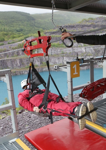 People lying horizontally in safety gear about to take off on a zip wire across a lake.