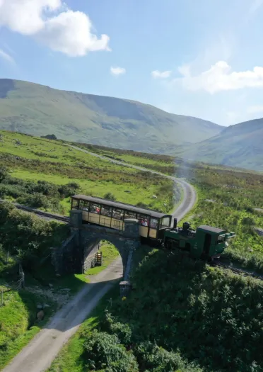 Diesel going over a bridge above a footpath leading up to a mountain summit.