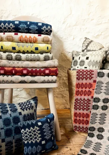Colourful woven blankets and cushions on display by a stool.