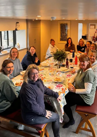Group of women sitting around a dining table smiling at the camera.