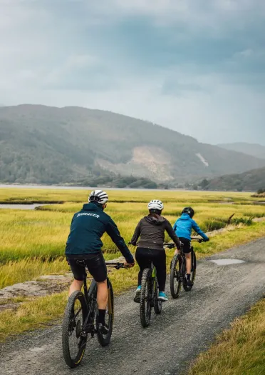 Family of cyclists on a path with mountains in the distance.
