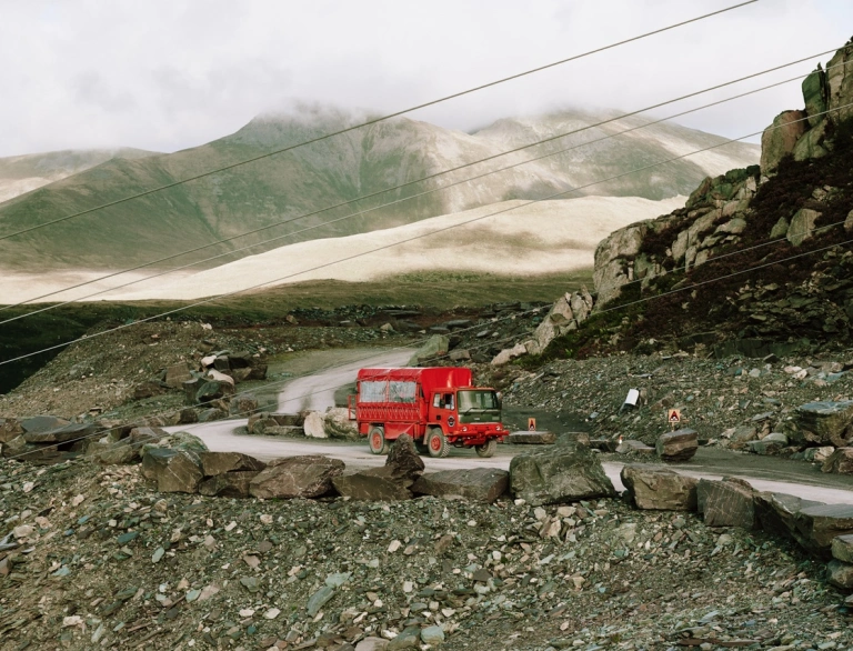 A red touring truck driving through a quarry.